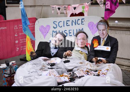 London, Großbritannien. November 2021. Aktivisten, die als Adani-Vorsitzender Gautam Adani, Science Museum Director Ian Blatchford und Shell-CEO Ben van Beurden gekleidet sind, liegen auf einem Bett mit gefälschtem Geld, Kohle und gefälschtem Öl, Während der Demonstration veranstalteten Extinction Rebellion Aktivisten einen Protest gegenüber dem Science Museum in South Kensington gegen die Patenschaft des Museums durch die fossilen Energiekonzerne Shell und Adani. Kredit: SOPA Images Limited/Alamy Live Nachrichten Stockfoto