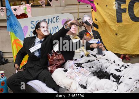 London, Großbritannien. November 2021. Aktivisten, die als Adani-Vorsitzender Gautam Adani, Science Museum Director Ian Blatchford und Shell-CEO Ben van Beurden gekleidet sind, liegen auf einem Bett mit gefälschtem Geld, Kohle und gefälschtem Öl, Während der Demonstration veranstalteten Extinction Rebellion Aktivisten einen Protest gegenüber dem Science Museum in South Kensington gegen die Patenschaft des Museums durch die fossilen Energiekonzerne Shell und Adani. Kredit: SOPA Images Limited/Alamy Live Nachrichten Stockfoto