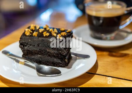 Fudgy reichen dunklen Schokolade Kuchen auf Platte mit Kaffee und Löffel Stockfoto