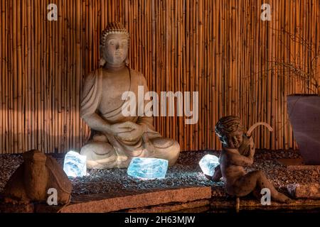 buddha-Figur und Engel im Garten, beleuchtet Stockfoto