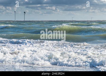 Mäßige Brandung mit teilweise bewölktem Himmel am Nordseestrand bei neeltje jans. Im Hintergrund einige Windturbinen. Stockfoto