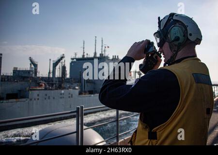 GOLF VON OMAN (NOV 11, 2021) Ens. Ian Murray benutzt einen Entfernungsmesser an Bord des amphibischen Angriffsschiffs USS Essex (LHD 2) während einer Auffüllung auf See mit dem Trocken- und Munitionsschiff USNS Cesar Chavez (T-AKE 14), November 11. Essex und die 11. Marine Expeditionary Unit werden im Einsatzgebiet der 5. US-Flotte eingesetzt, um Marineoperationen zu unterstützen, um die maritime Stabilität und Sicherheit in der Zentralregion zu gewährleisten und das Mittelmeer und den Pazifik durch den westlichen Indischen Ozean und drei strategische Engpässe zu verbinden. (USA Navy Foto von Mass Communication Specialist 2nd Class John Mc Stockfoto