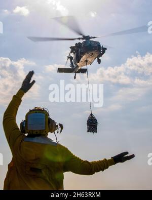GOLF VON OMAN (NOV 11, 2021) Aviation Boatswain's Mate (Handling) 2nd Class Dominique Simmons signalisiert einem MH-60S Sea Hawk Hubschrauber, der an das Hubschrauber Sea Combat Squadron 21 an Bord des amphibischen Sturmschiffs USS Essex (LHD 2) während einer vertikalen Nachfüllung auf See mit dem Trockenfracht- und Munitionsschiff USNS Cesar Chavez (T-AKE 14) angebracht ist, Nov. 11. Essex und die 11. Marine Expeditionary Unit werden im Einsatzgebiet der 5. US-Flotte eingesetzt, um Marineinteroperationen zu unterstützen, um die maritime Stabilität und Sicherheit in der Zentralregion zu gewährleisten und das Mittelmeer und den Pazifik durch t zu verbinden Stockfoto