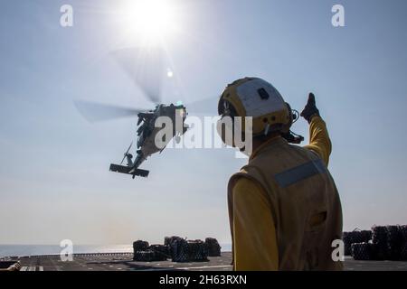 GOLF VON OMAN (NOV 11, 2021) der Mate (Handling) der 2. Klasse von Aviation Boatswain, Cody McCracken, sendet Signale an einen an das Sea Combat Squadron 21 des Hubschraubers MH-60S befestigten Sea Hawk-Hubschrauber an Bord des amphibischen Sturmschiffs USS Essex (LHD 2) während einer vertikalen Auffüllung auf See mit dem Trocken- und Munitionsschiff USNS Cesar Chavez (T-AKE 14), Nov. 11. Essex und die 11. Marine Expeditionary Unit werden im Einsatzgebiet der 5. US-Flotte eingesetzt, um Marineinteroperationen zu unterstützen, um die maritime Stabilität und Sicherheit in der Zentralregion zu gewährleisten und das Mittelmeer und den Pazifik über die zu verbinden Stockfoto