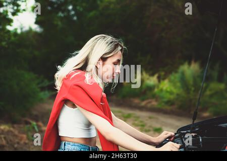 Mädchen schaut unter die Haube eines kaputten Autos. Weicher, selektiver Fokus. Stockfoto