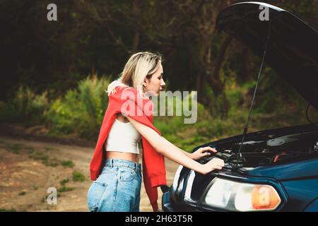 Mädchen schaut unter die Haube eines kaputten Autos. Weicher, selektiver Fokus. Stockfoto