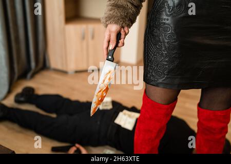 Nahaufnahme des Mittelabschnitts einer unbekannten Mörderin mit blutigem Messer, wobei ein unbekannter Mann tot auf dem Boden liegt und mit Geldscheinen gestochen wurde aro Stockfoto