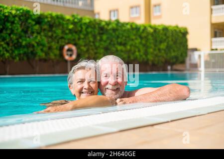 Ein paar von zwei glücklichen Senioren, die Spaß haben und gemeinsam im Schwimmbad genießen lächeln und auf die Kamera schauen. Glückliche Menschen genießen den Sommer im Freien im Wasser Stockfoto