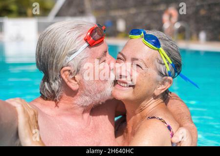 Zwei glückliche Senioren, die Spaß haben und gemeinsam im Schwimmbad ein Selfie-Foto machen, lächeln und auf die Kamera schauen. Glückliche Menschen, die den Sommer draußen im Wasser genießen Stockfoto