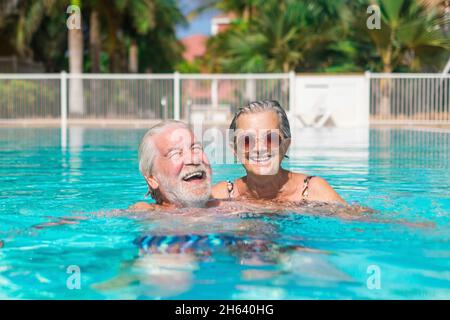 Ein paar von zwei glücklichen Senioren, die Spaß haben und gemeinsam im Schwimmbad genießen, lächeln und spielen. Glückliche Menschen genießen den Sommer im Freien im Wasser Stockfoto