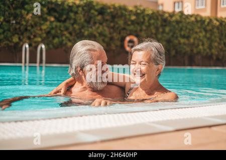 Ein paar von zwei glücklichen Senioren, die Spaß haben und gemeinsam im Schwimmbad genießen, lächeln und spielen. Glückliche Menschen genießen den Sommer im Freien im Wasser Stockfoto