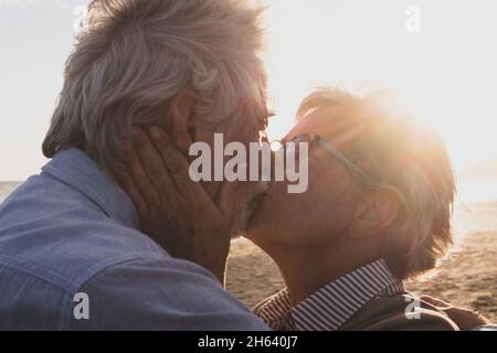 Porträt und Nahaufnahme von zwei verliebten Senioren, die lächelnd mit der Sonne des Sonnenuntergangs zwischen ihren Köpfen tanzen Stockfoto