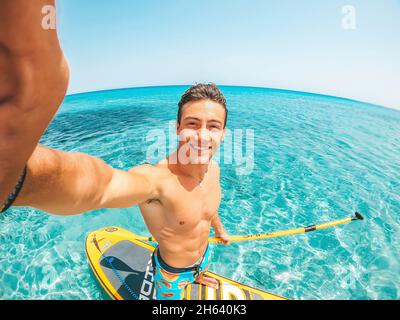 Ein glücklicher kaukasischer Mann genießt und Spaß im Urlaub im Freien am Strand Reiten einer Paddel-Brandung im Wasser. Attraktiver Junge fühlen sich frei reisen. Stockfoto