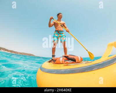 Ein glücklicher kaukasischer Mann genießt und Spaß im Urlaub im Freien am Strand Reiten einer Paddel-Brandung im Wasser. Attraktiver Junge fühlen sich frei reisen. Stockfoto