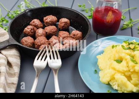 Hausgemachte Schwedenfleischbällchen in gusseiserner Pfanne serviert mit Kartoffelpüree und Rotbeersauce mit zwei Gabeln, Seitenansicht aus der Nähe Stockfoto