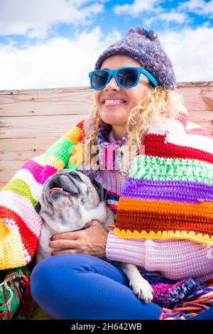 Glückliche Frau genießen ihren Mops Hund sitzen draußen zu Hause im Winter mit bunten Abdeckungen - Zärtlichkeit und Freundschaft Menschen Tierkonzept Lifestyle - fröhlich hübsche weibliche Lächeln Porträt Stockfoto