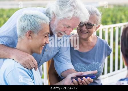 Großeltern mit Enkel mit Blick auf Handy. Glückliche Multi-Generation-Familie Blick auf die Rückseite eines Mobiltelefons Gerät. Stockfoto