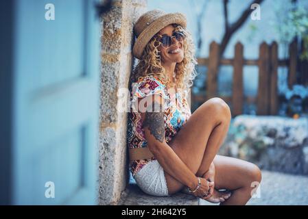 Porträt einer schönen lächelnden Hipster junge Frau in Sonnenbrillen und Strohhut sitzen im Freien. Stilvolle tätowierte Frau in guter Laune verbringen Freizeit im Freien entspannen Stockfoto