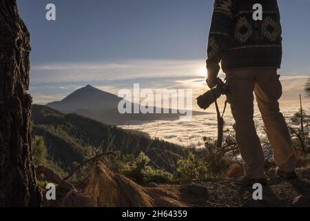 Fotograf Mann mit dslr-Kamera bewundern szenische Bergblick und Himmel. Wanderer bewundern atemberaubende Bergkette. Tourist mit Kamera bewundern atemberaubende Landschaft über Berggipfel. Stockfoto