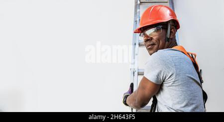 Dienstleister mit Helm, der eine Metallleiter klettert. Bauarbeiter. Lateinischer Mann. Stockfoto