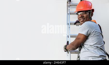 Dienstleister mit Helm, der eine Metallleiter klettert. Bauarbeiter. Lateinischer Mann. Stockfoto