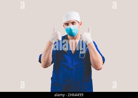 Junger Arzt mit Daumen nach oben in blauem Chirurgen-Anzug und Brille mit Stethoskop auf gelbem Hintergrund isoliert Stockfoto