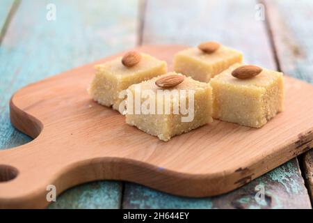Hausgemachte leckere Grieß Halva mit ganzen Mandeln in Quadrate auf Holzbrett geschnitten. Traditionelle indische Süßigkeiten aus der Nähe Stockfoto