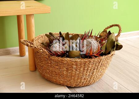 Korbkorb mit exotischen getrockneten Blumen in der Nähe der grünen Wand Stockfoto