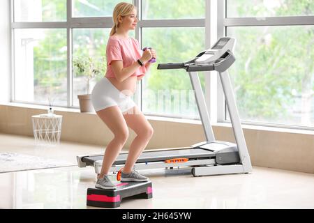 Junge Schwangeren trainieren mit Aerobic-Stepper und Kurzhanteln im Fitnessstudio Stockfoto