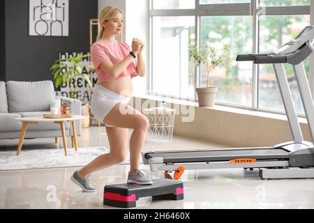 Junge Schwangerin trainiert zu Hause mit Aerobic Stepper Stockfoto