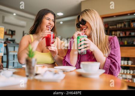 Junge Latein plus size Mädchen sitzen im Café und hören lustige Lebensgeschichte von ihrem Freund Stockfoto