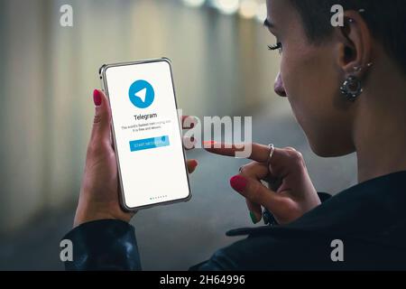 Eine junge hübsche Frau startet einen modernen Telegrammboten. Telegramm-Logo und Tasten auf dem Startbildschirm des Smartphones. 22. Juli 2018. Barnaul, Russland. Stockfoto