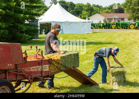 Zwei Jungbauern demonstrieren auf einer Traktorenschau in Warren, Indiana, USA, den Einsatz einer antiken Heuballenpresse des Typs 271 aus New Holland. Stockfoto