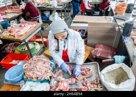 Eine kasachische Frau schneidet Pferdefleisch, um Qazy, Pferdewurst, auf dem Fleischmarkt Altyn Orda, Almaty, Kasachstan zuzubereiten Stockfoto