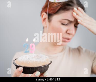 Unglückliche Frau hält einen Kuchen mit Kerzen für ihren 29. Geburtstag. Das Mädchen weint über den Verlust der Jugend. Stockfoto