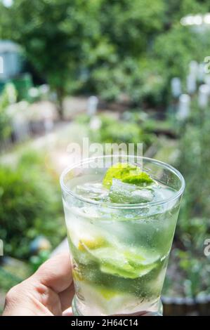 Ein erfrischender Mojito-Drink in der Hand einer Frau. Vertikal, im Freien, an einem sonnigen Sommertag. Stockfoto