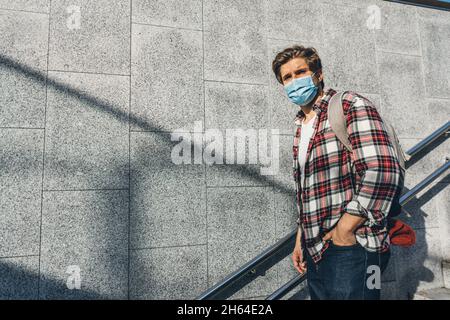 Junger Mann mit Schutzmaske auf seinem Gesicht, der in der U-Bahn die Treppe hinunter ging. Hipster-Typ auf einer Stadtstraße Stockfoto