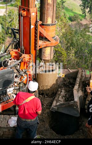 Ferngesteuerter Bagger bohrt ein tiefes Loch in die Erde für ein neues Betonfundament am Hang Stockfoto