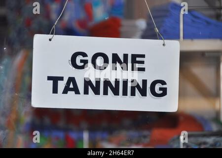 Nahaufnahme eines Schildes an der Glastür eines Ladens, das die Kunden darüber informiert, dass das Geschäft (vorübergehend) geschlossen ist und eine Meldung über die Bräunung angezeigt wird Stockfoto