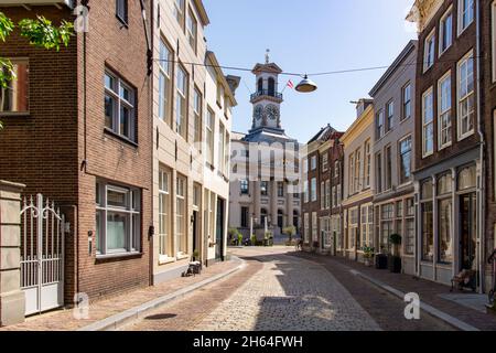 Dordrecht, Niederlande-Juli 2021; Blick über die kopfsteingepflasterte Straße von Grotekerksebuurt, gesäumt von historischem Gebäude und Rathaus mit ikonischer Uhr Stockfoto