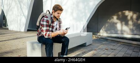 Porträt eines modernen jungen Mannes mit Smartphone auf einer Straße. Hipster Kerl mit Handy in der Hand im Freien Stockfoto