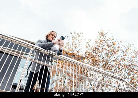 Moderner Geschäftsmann mit Smartphone in den Händen auf einer Stadtstraße. Schöner Mann, der Ohrhörer trägt und auf dem Mobiltelefon spricht, Musik hört oder Podc hört Stockfoto