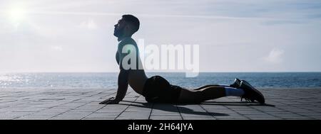 Fit junger Mann Stretching nach dem Training im Freien. Männlicher Athlet, der morgens während des Lockdown vor dem Fitnessstudio Fitnesstraining macht. Stockfoto
