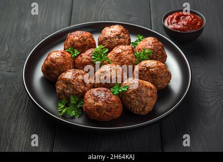 Gebratene Fleischbällchen in Nahaufnahme auf einem schwarzen Teller auf dunklem Hintergrund mit Tomatensauce. Seitenansicht. Stockfoto