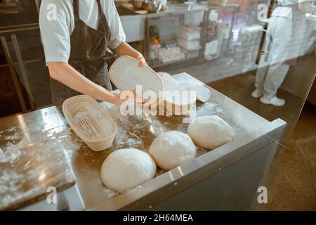 Baker deckt die innere Oberfläche der Schale für Brot mit Mehl in der Werkstatt Stockfoto