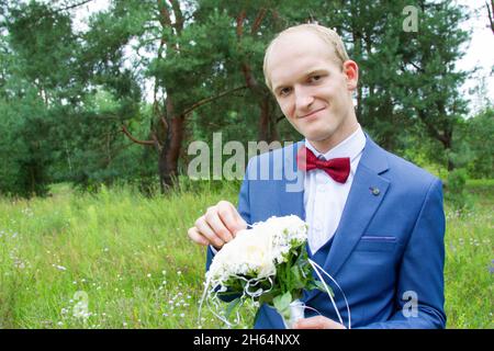 Porträt des Bräutigams mit europäischem Aussehen in einem blauen Hochzeitsanzug mit einem Blumenstrauß. Stockfoto