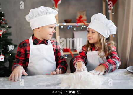 Fröhlicher Bruder Schwester machen Teig für Weihnachtskekse, Kinder in der Küche bereiten Lebkuchen, kleine Köche. Weihnachtliches Essen Stockfoto