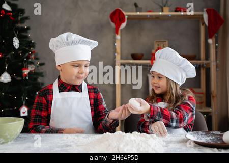 Glückliche Kinder in der Küche machen Teig für Weihnachtskekse, eine Familie in der Küche bereitet Lebkuchenkuchen zu, kleine Köche brechen ein Ei. Stockfoto