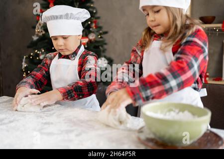 Familie, Kinder bereiten Weihnachtsplätzchen zu, Bruder und Schwester kneten Teig auf dem Tisch, Lebkuchenkochen, Essen zubereiten Stockfoto