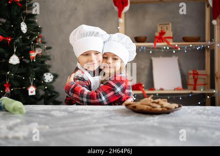 Kinder Bäcker Bruder und Schwester machte hausgemachte Weihnachtsplätzchen in der Küche. Ein Junge und ein Mädchen in einer Kochmütze und Schürze mit Lebkuchen Stockfoto